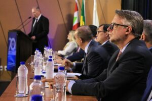 Banner horizontal com foto de perfil do procurador-geral em exercício, Diogo Ringenberg, ao lado das demais autoridades na bancada no palco do auditório do TCE/SC, durante cerimônia de posse. Ele é um homem branco, de cabelos grisalhos. Veste terno e gravata e usa óculos de grau.