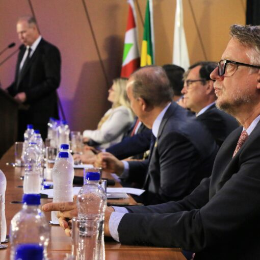 Banner horizontal com foto de perfil do procurador-geral em exercício, Diogo Ringenberg, ao lado das demais autoridades na bancada no palco do auditório do TCE/SC, durante cerimônia de posse. Ele é um homem branco, de cabelos grisalhos. Veste terno e gravata e usa óculos de grau.